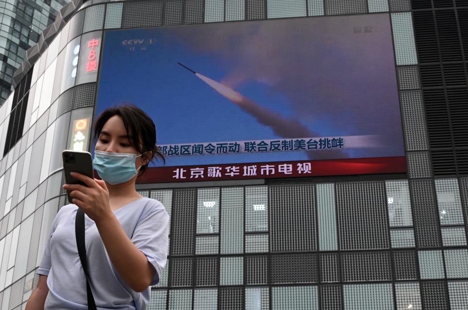 Uma mulher em Pequim mexe no celular enquanto uma tela grande mostra os exercícios militares da China cercando Taiwan (Foto: NOEL CELIS/AFP via Getty Images)