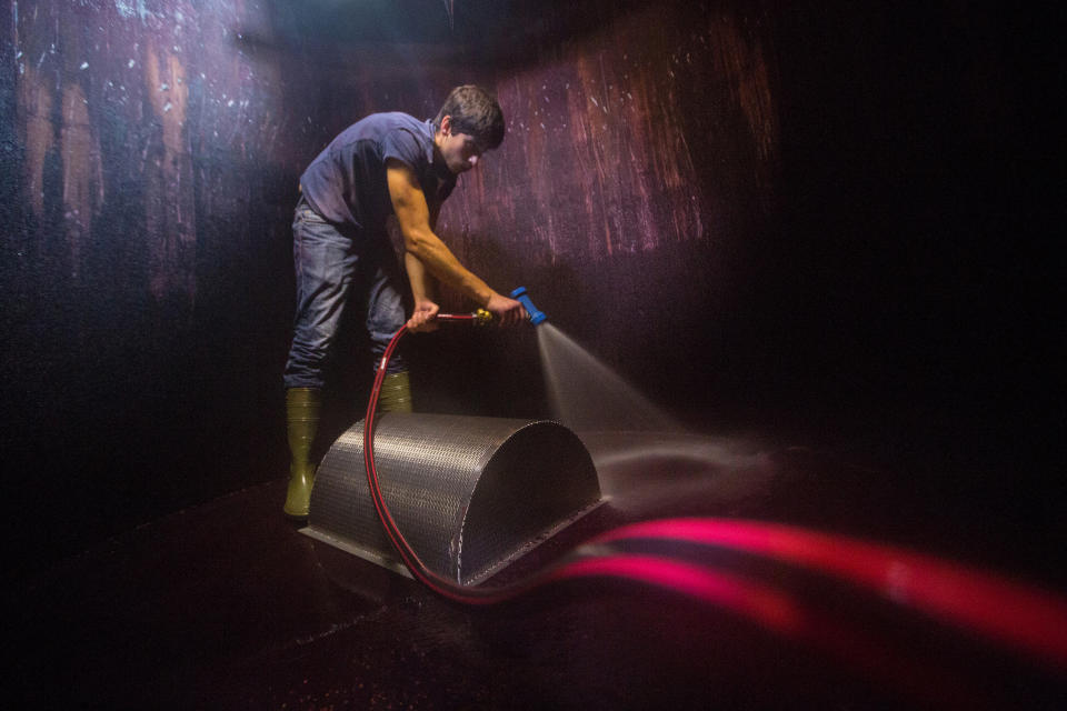 A worker uses a high pressure water hose to clean a fermentation tank.