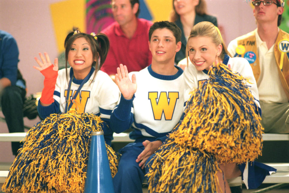 Brenda Song, Ricky Ullman, and Alyson Michalka sit in bleachers dressed as cheerleaders