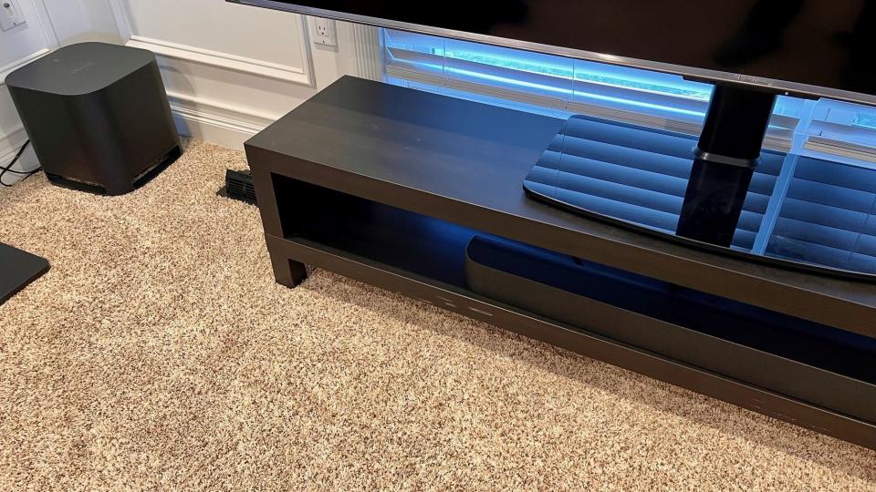 A photo of the Roku Wireless Bass Pro subwoofer (left) alongside a TV stand with the Streambar Pro.