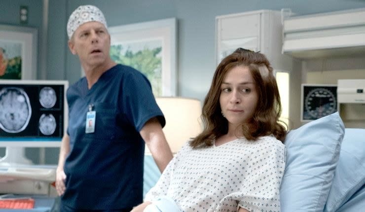 A still from Grey's Anatomy showing Amelia in a hospital bed, Dr Koracick standing behind her with scans of her brain on a computer