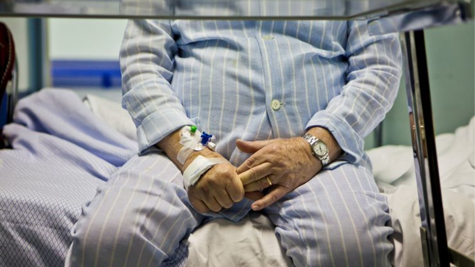 Um homem idoso sentado em uma cama de hospital