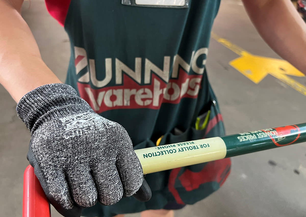 Bunnings worker's gloved hand on trolley, apron visible in background