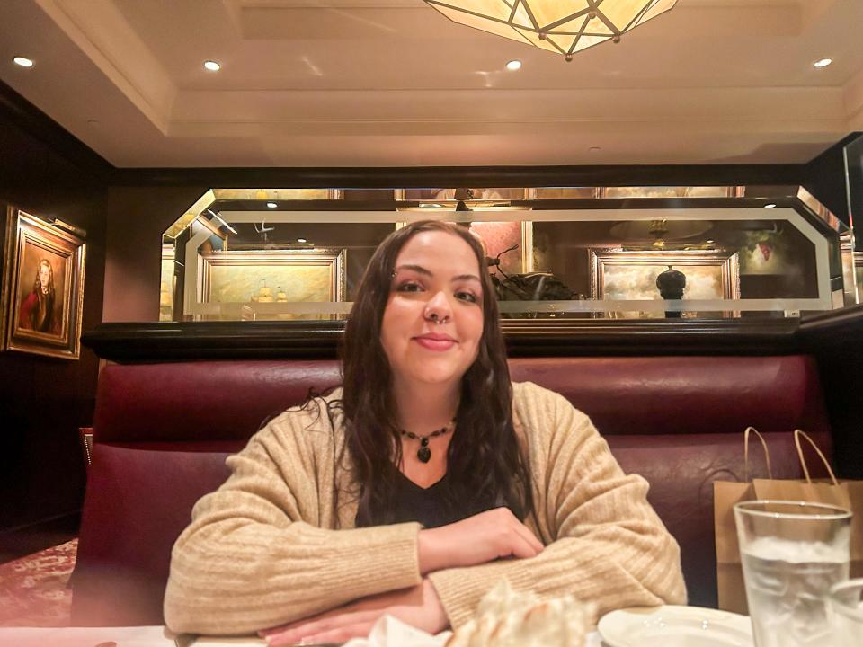 Amena, wearing a black shirt and a cardigan, sits in a booth at The Capital Grille.