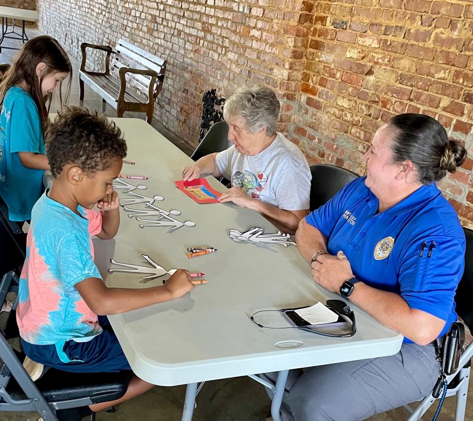 Attendees of a “My Community, My Responsibility” program held July 11, 2023, in Collinsville, Alabama, color paper dolls while talking with Rebecca Clayton and Ada Hamilton at the Collinsville Public Library.