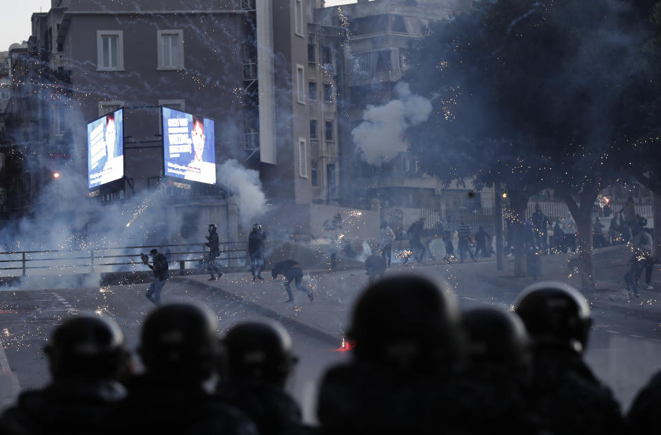 Supporters of the Shiite Hezbollah and Amal Movement groups, background, clashes with the riot policemen, foreground, as they trying to attack the anti-government protesters squares, in downtown Beirut, Lebanon, Saturday, Dec. 14, 2019. Lebanon has been facing its worst economic crisis in decades, amid nationwide protests that began on Oct.17 against the ruling political class which demonstrators accuse of mismanagement and corruption. (AP Photo/Hussein Malla)