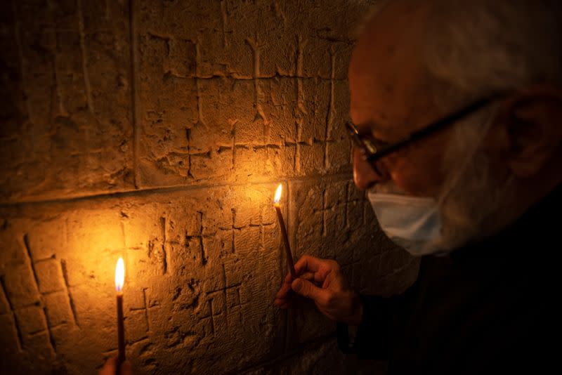 Father Samuel Aghoyan, the Armenian superior at the Church of the Holy Sepulchre holds candles to illuminate crosses etched into the ancient stone wall of the Saint Helena chapel inside the church, during his interview with Reuters, in Jerusalem's Old City