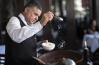 Salad Master Efrain Montoya tosses in Parmesan cheese as he prepares a Caesar salad at Ceasar's restaurant Thursday, June 27, 2024, in Tijuana, Mexico. Caesar salad has something to celebrate: It's turning 100. Italian immigrant Caesar Cardini is said to have invented the dish on July 4, 1924, at his restaurant, Caesar's Place, in Tijuana, Mexico. (AP Photo/Gregory Bull)