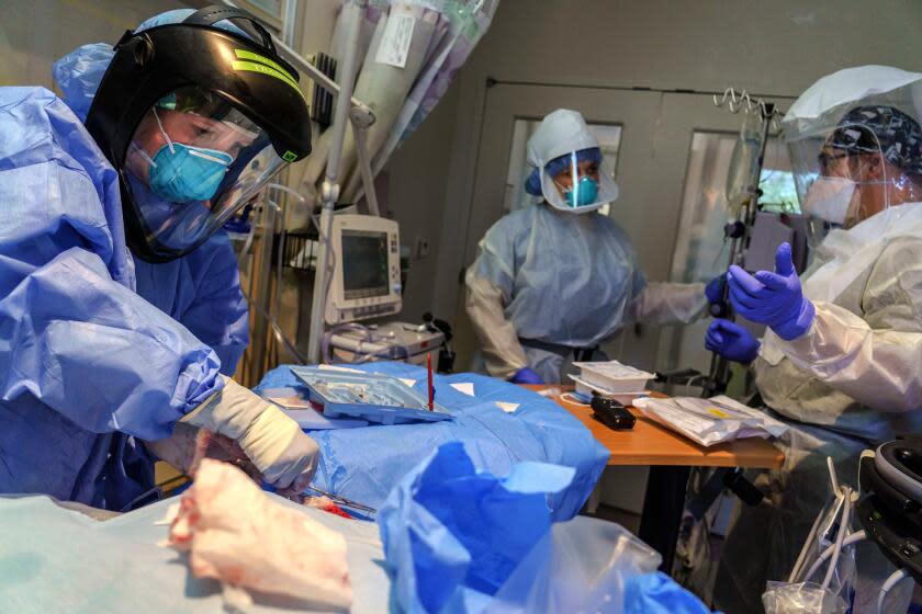 CHULA VISTA, CALIF. -- THURSDAY, APRIL 23, 2020: From left to right: Nurse Practitioner Charlotte Thomas, respiratory therapist Sandra Sandoval and registered nurse Saul Reynoso work on stabilizing a COVID-19 patient by placing central vascular lines after the patient was intubated, inside a negative pressure isolation room at the ICU at Scripps Mercy Hospital in Chula Vista, Calif., on April 23, 2020. (Marcus Yam / Los Angeles Times)