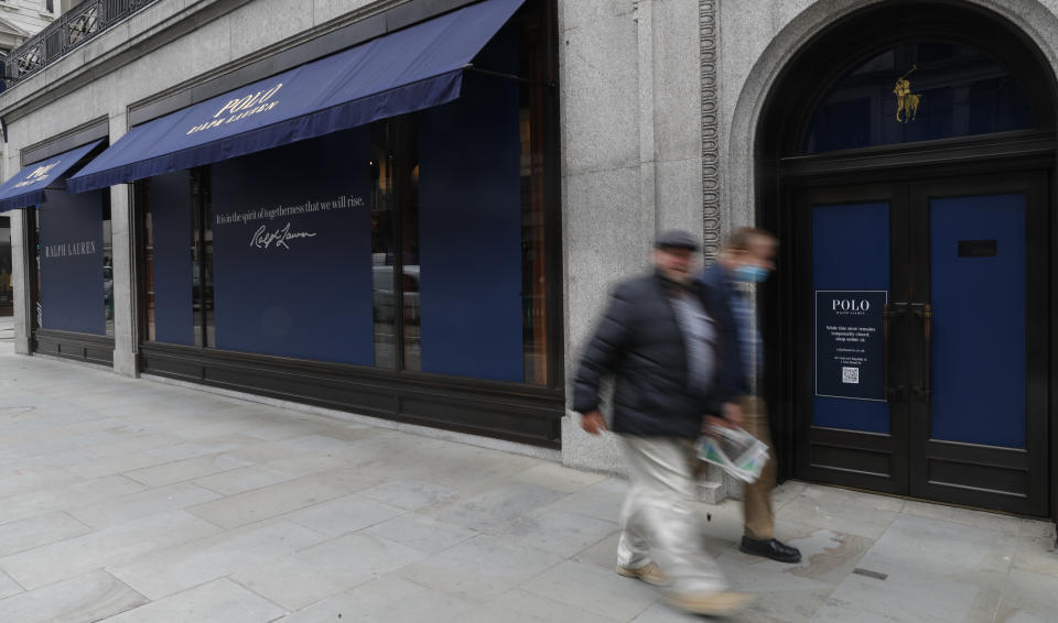 Men walk by a closed Ralph Lauren store in London, Thursday, July 16, 2020. Unemployment across the U.K. has held steady during the coronavirus lockdown as a result of a government salary support scheme, but there are clear signals emerging that job losses will skyrocket over coming months. The Office for National Statistics said Thursday there were 649,000 fewer people, or 2.2%, on payroll in June when compared with March when the lockdown restrictions were imposed. (AP Photo/Alastair Grant)