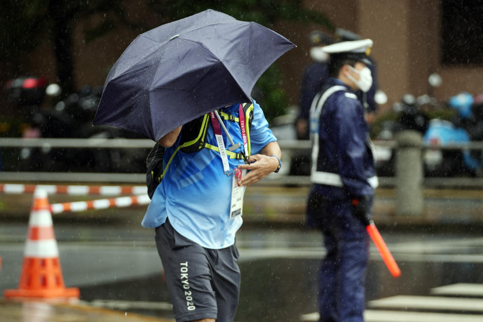 An Olympic worker holds an umbrella against strong wind and rain prior to the women's triathlon competition at the 2020 Summer Olympics Tuesday, July 27, 2021, in Tokyo, Japan. (AP Photo/Eugene Hoshiko)