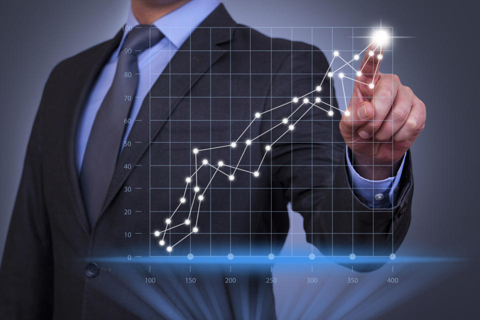 Man in a suit pointing to an upward trending series of data points on a graph.