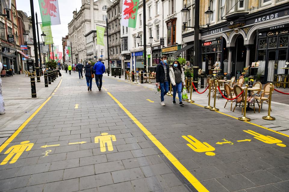 People wear face coverings as they walk along socially distanced floor markings in Cardiff after the Welsh Government placed three more areas of Wales into local lockdown.PA