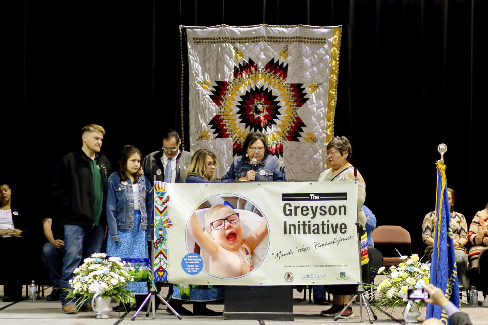 In this photo provided by LifeSource, Joan Azure, the grandmother of Greyson Parisien, center, speaks at an event in Belcourt, N.D., on Monday, Nov. 14, 2022, where the Turtle Mountain Band of Chippewa Indians unveiled an identification card that has a spot to designate organ donation. Tribal member Greyson Parisien, who had a heart transplant, inspired the change. The Turtle Mountain Band of Chippewa is the first tribal nation to offer donor registration on tribal identification cards. (Mike Hutto/LifeSource via AP)