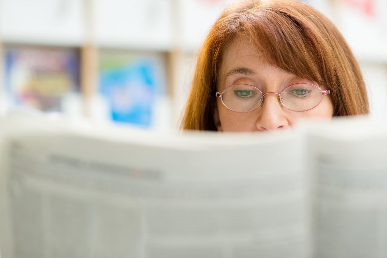 middle aged woman with eyeglasses reading paper in library