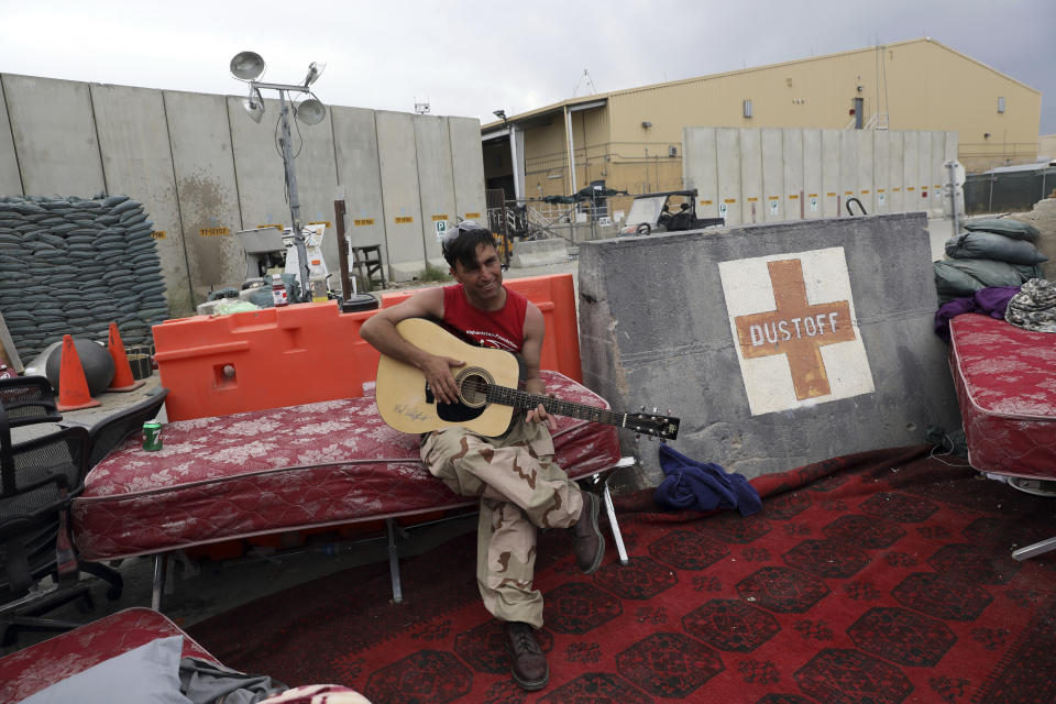 An Afghan soldier plays a guitar that was left behind after the American military departed Bagram air base, in Parwan province north of Kabul, Afghanistan, Monday, July 5, 2021. The U.S. left Afghanistan's Bagram Airfield after nearly 20 years, winding up its "forever war," in the night, without notifying the new Afghan commander until more than two hours after they slipped away. (AP Photo/Rahmat Gul)