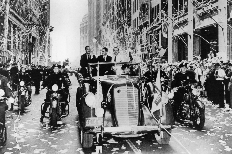 Howard Hughes sits in a car and waves to the crowd as he celebrates his success in a parade in 1938.
