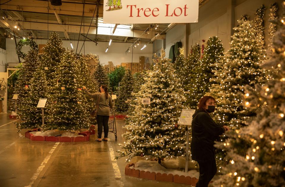 An indoor storage space filled with plastic Christmas trees and two shoppers wearing masks.