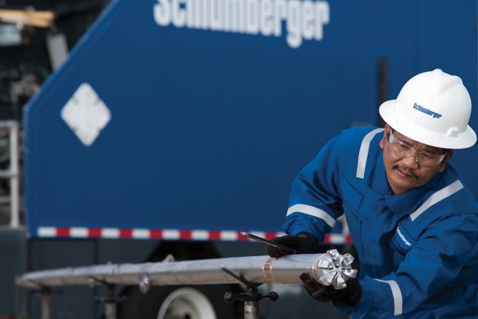 A worker wearing a Schlumberger hard hat pulling a drill bit out of a trailer