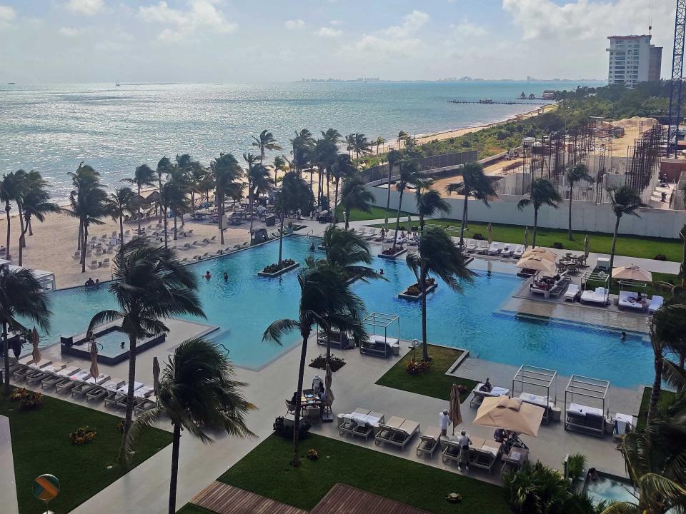 A shot of a hotel pool next to the beach and ocean with palm trees and views of the coast.