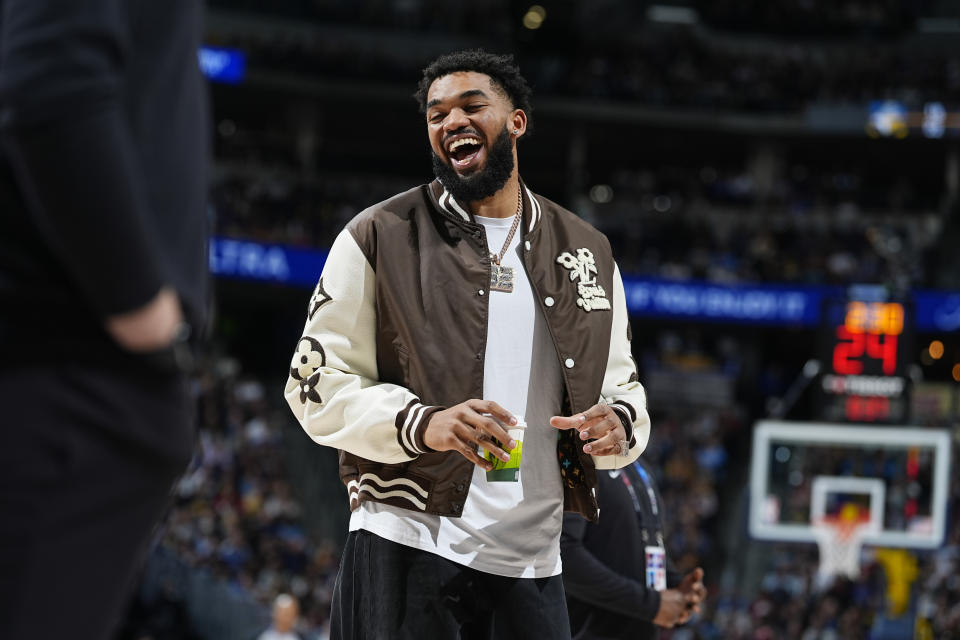 Injured Minnesota Timberwolves center Karl-Anthony Towns jokes with teammates during the first half of the team's NBA basketball game against the Denver Nuggets on Wednesday, April 10, 2024, in Denver. (AP Photo/David Zalubowski)