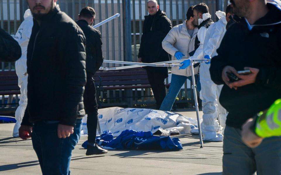 Police forensic team wait with the bodies of the attackers after they were shot dead outside the building