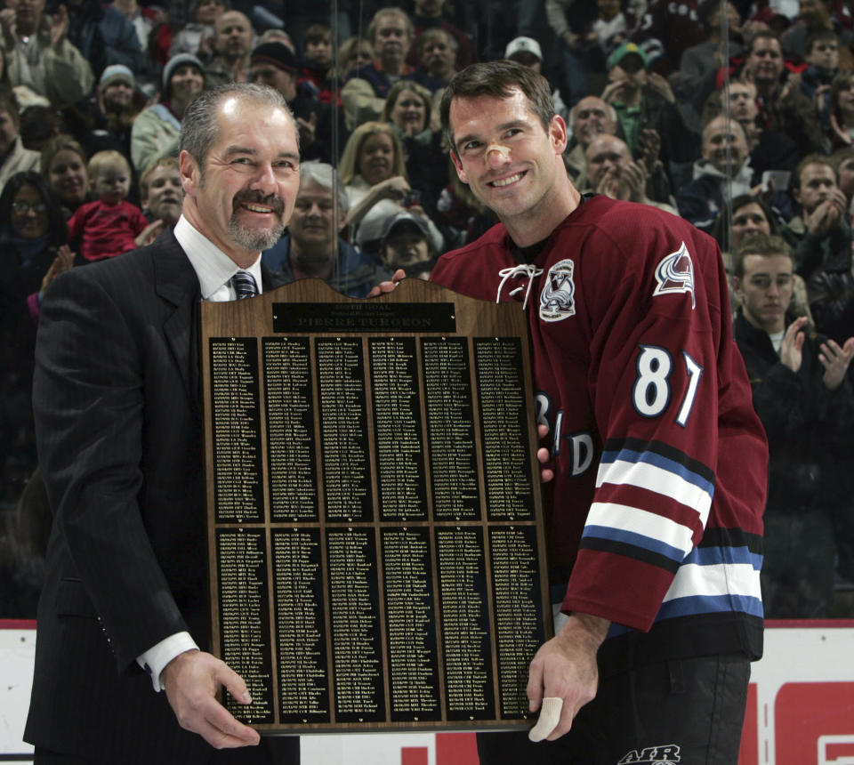 FILE - Michel Goulet, left, special assistant to the president of the Colorado Avalanche Hockey Club, presents a plaque detailing all 500 of the NHL goals scored by Avalanche center Pierre Turgeon, right, in a ceremony before the Avalanche hosted the Buffalo Sabres in Denver, on Sunday, Dec. 4, 2005. Turgeon is one of five players elected to the Hockey Hall of Fame, Wednesday, June 21, 2023. (AP Photo/David Zalubowski, File)