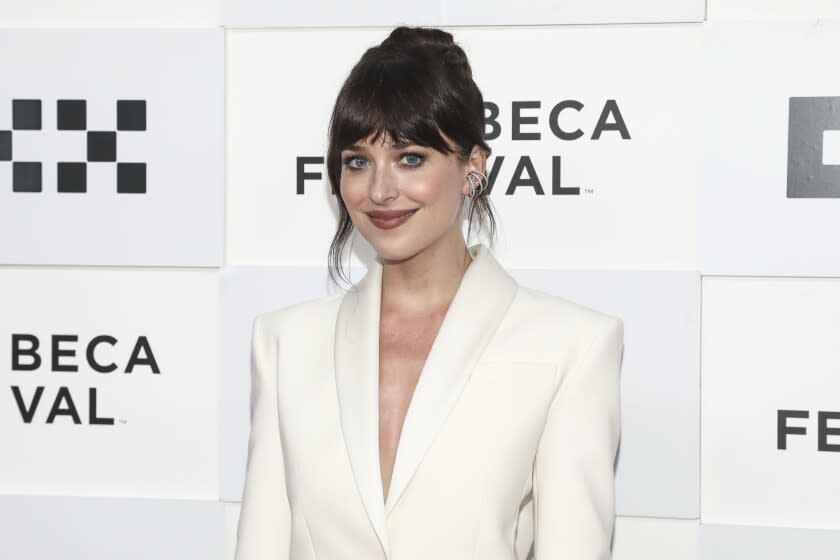 A woman with brown hair and bangs wears a white suit. She poses for pictures at a red carpet event.