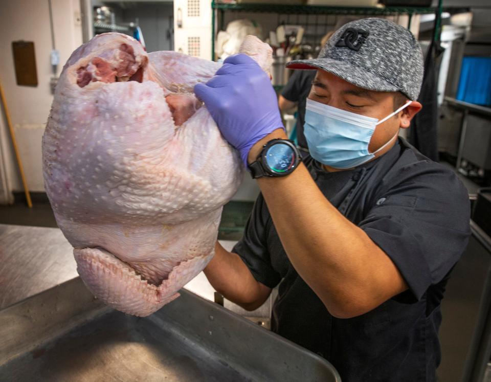 Eugene Mission assistant chef Tino Mendoza-Cruz wrestles a 42-pound turkey into the pan as preparation for a free community Thanksgiving meal are underway at the Eugene non-profit.