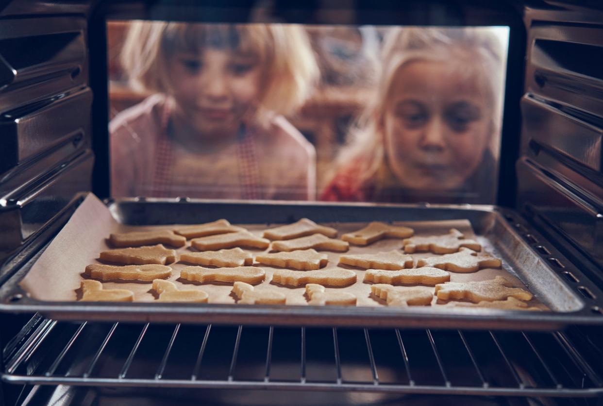 Young girls watch as cookies bake in the oven. 