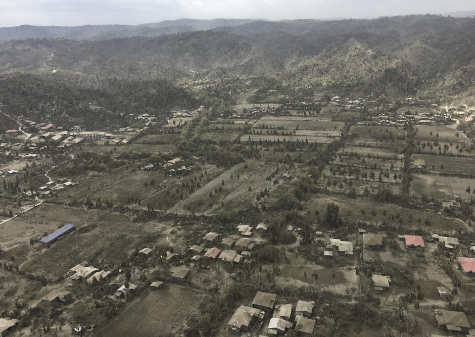 In this Jan. 21, 2020, handout aerial photo provided by the Office of Civil Defense, volcanic ash covers roofs of houses and land near Taal volcano in Batangas province, southern Philippines. The government will no longer allow people to live on the crater-studded island that's home to Taal volcano. (Office of Civil Defense via AP)