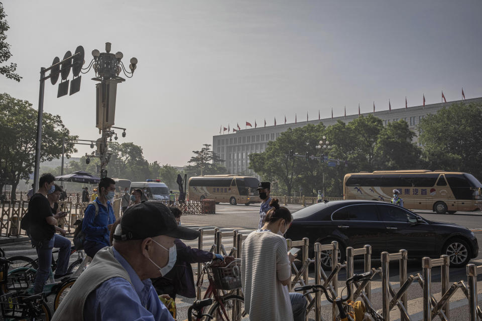 People wait behind a security fence as delegates' buses drive to the Great Hall of the People for the opening session of China's National People's Congress (NPC), in Beijing, China, Friday, May 22, 2020. (Roman Pilipey/Pool Photo via AP)