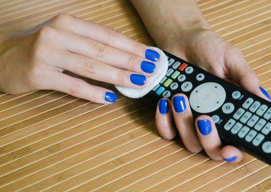 Woman with blue fingernails using a cotton circle to clean a remote control