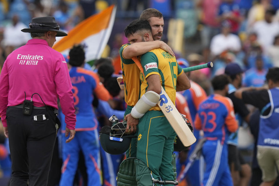 South Africa's Anrich Nortje consoles teammate Keshav Maharaj as India's players celebrate their win against South Africa in the ICC Men's T20 World Cup final cricket match at Kensington Oval in Bridgetown, Barbados, Saturday, June 29, 2024. (AP Photo/Ramon Espinosa)