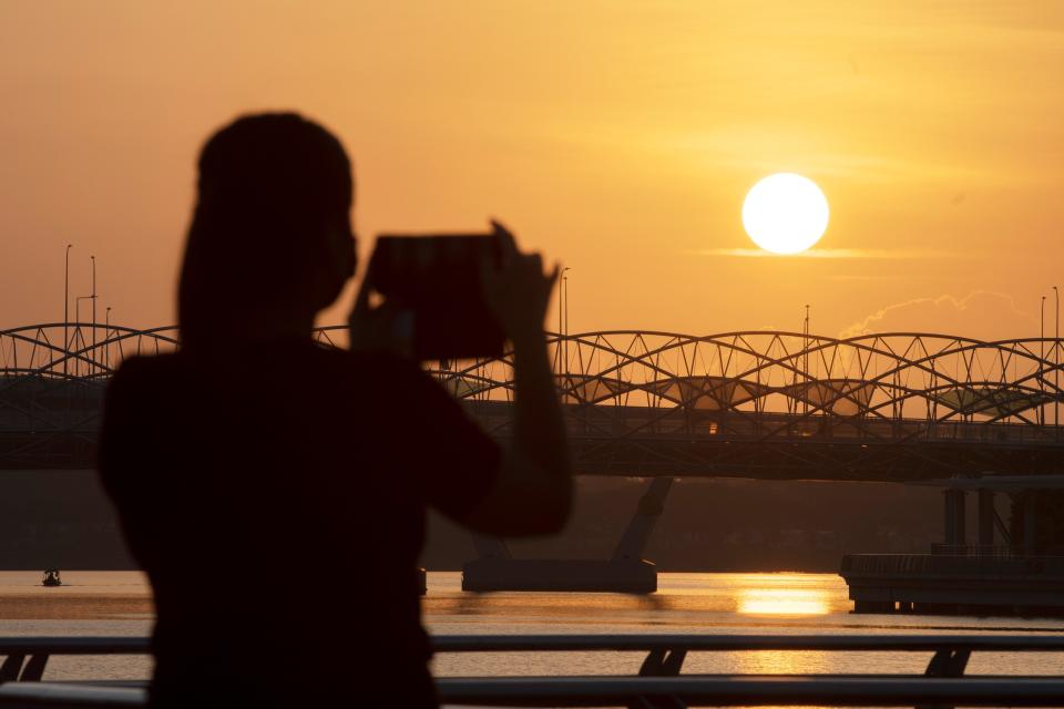 SINGAPORE, March 16, 2021 -- A woman takes photos of the sunrise at the Merlion Park in Singapore, on March 16, 2021. (Photo by Then Chih Wey/Xinhua via Getty) (Xinhua/Then Chih Wey via Getty Images)