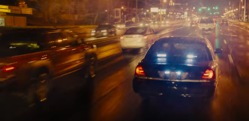 A car races in the rain down a busy street