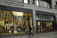 A person wearing a face mask to try to curb the spread of coronavirus walks past the temporarily closed Topshop flagship store on Oxford Street, during England's second coronavirus lockdown, in London, Monday, Nov. 30, 2020. Arcadia Group, the retail empire of tycoon Philip Green, which owns well-known British fashion chains like Topshop and employs around 15,000 people, appears to be on the brink of collapse following the economic shock of the coronavirus pandemic. (AP Photo/Matt Dunham)