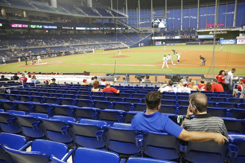 FILE - In this Monday, Aug. 26, 2019 file photo, fans watch play among empty seats during the second inning of a baseball game between the Miami Marlins and the Cincinnati Reds in Miami. Many college and pro sports teams already were dealing with declining ticket sales. The improved at-home experience, the emergence of wide-spread legalized betting and the changing social makeup of fan bases have been catalysts, while dynamic pricing, increases in parking and concession prices and a push toward luxury seating have exacerbated the problem. (AP Photo/Wilfredo Lee, File)