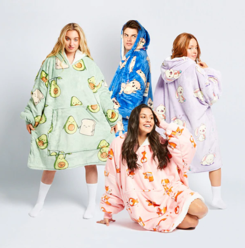 Four young people strike poses while wearing different Oodie tops in patterns of avocado, dogs and cartoon characters in shades of blue, green, mauve and pink.