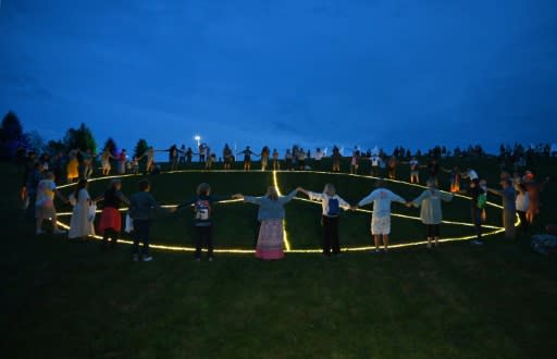 Guests hold hands around a giant illuminated peace sign during the 50th anniversary celebration of Woodstock at Bethel Woods Center for the Arts