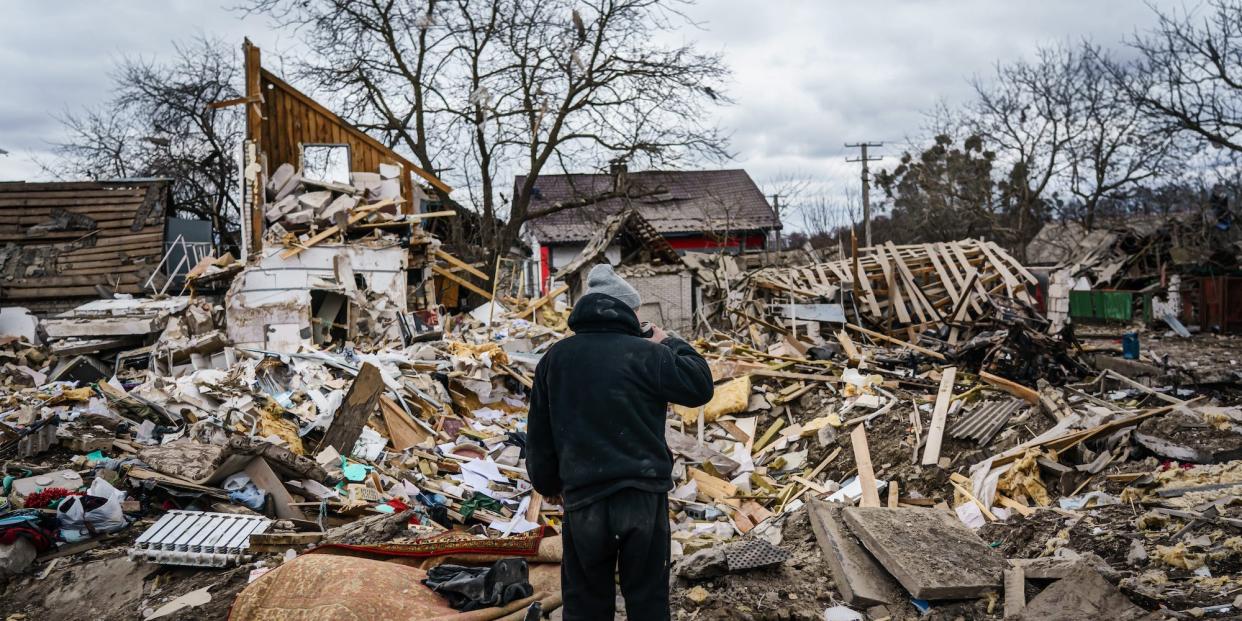 A man in black with his back to the camera, facing the wreckage of his home in Ukraine, March 5 2022.