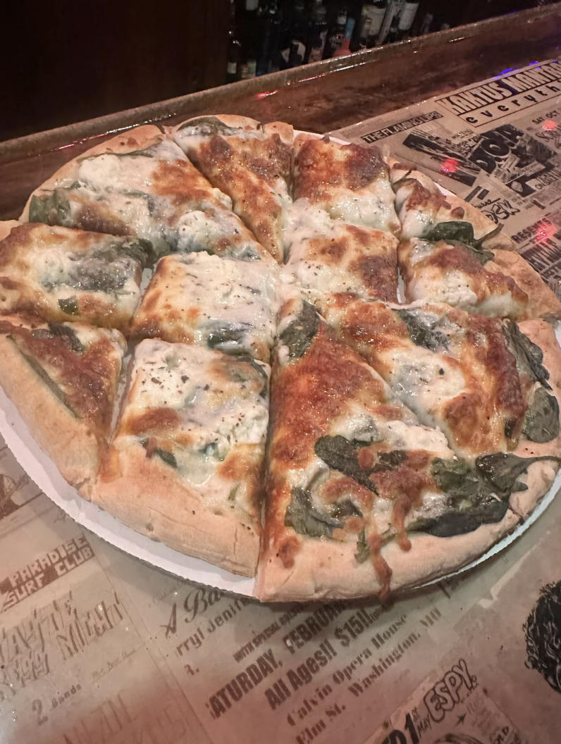 A sliced pizza with melted cheese and spinach toppings on a wooden table