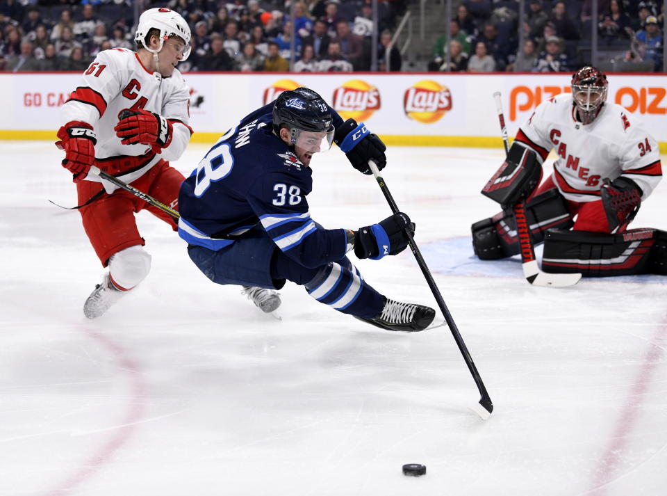 Winnipeg Jets' Logan Shaw (38) and Carolina Hurricanes' Jake Gardiner (51) battle for the puck in front of goaltender Petr Mrazek (34) during second period NHL hockey action in Winnipeg, Manitoba on Tuesday Dec. 17, 2019. (Fred Greenslade/The Canadian Press via AP)