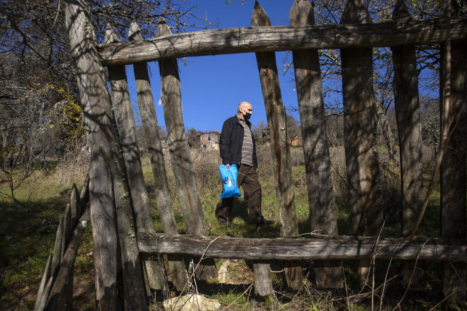 Kosovo Albanian Fadil Rama seen through damaged wooden fence in the deserted village carrying groceries to the only resident Kosovo Serb Blagica Dicic a lonely 92-year old woman in a remote village of Vaganesh, Kosovo on Thursday, Nov. 19, 2020, abandoned by all her former ethnic Serb neighbors. Neighbor Blagica Dicic, is 92 and in failing health, in the remote ethnic Serb minority village in the mountains of eastern Kosovo but Fadil Rama comes from the other side of Kosovo’s bitter ethnic divide, being a member of Kosovo’s ethnic Albanian majority and Rama said he saw nothing strange in helping an elderly Serb. “I will never leave her on her own,” he said. (AP Photo/Visar Kryeziu)