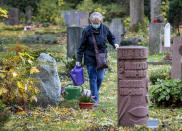 An elderly woman wearing a face mask takes care of a grave at the main cemetery in Frankfurt, Germany, Wednesday, Oct. 28, 2020. (AP Photo/Michael Probst)