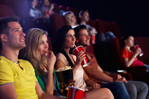 A group of young people eating popcorn and drinking soda at a movie theater.