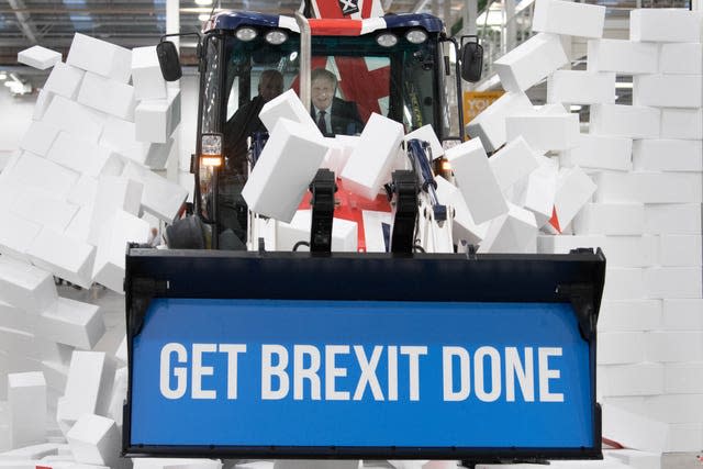 Boris Johnson drives a Union flag-themed JCB, with the words 'Get Brexit Done' inside the digger bucket, through a fake wall emblazoned with the word 'Gridlock'