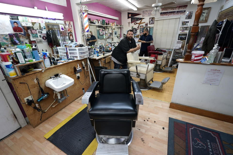 FILE - In this March 20, 2020 file photo, Carlos Vasquez, left, and his nephew R.J. Vasquez, wait for customers at their family's barber shop in Houston. Reaction to the coronavirus, change came to the United States during the third week of March in 2020. It did not come immediately, though it came quite quickly. There was no explosion, no invasion other than a microscopic one that nobody could see. (AP Photo/David J. Phillip, File)