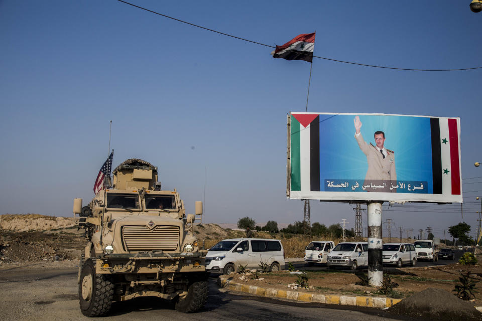 File - In this Saturday, Oct. 26. 2019 file photo, U.S. military convoy drives the he town of Qamishli, north Syria, by a poster showing Syrian President Bashar Aassad. Syrians are marking 10 years since peaceful protests against President Bashar Assad's government erupted in March 2011, touching off a popular uprising that quickly turned into a full-blown civil war. (AP Photo/Baderkhan Ahmad, File)