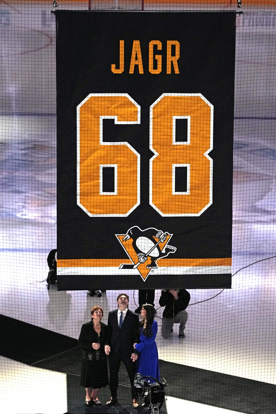 Former Pittsburgh Penguins player Jaromir Jagr, bottom center, along with his mother, left, and girlfriend watch as his uniform number is raised to the rafters of PPG Paints arena after being retired during a pregame ceremony before an NHL hockey game between the Los Angeles Kings and Pittsburgh Penguins in Pittsburgh, Sunday, Feb. 18, 2024. (AP Photo/Gene J. Puskar)